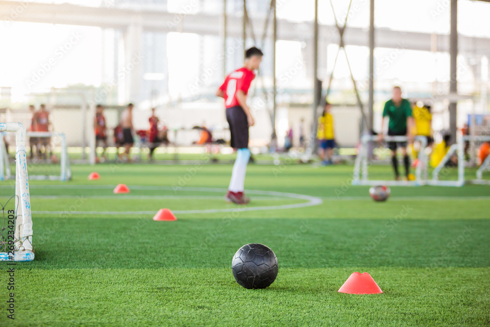 black football on green artificial turf with mini goal and blurry soccer team training,