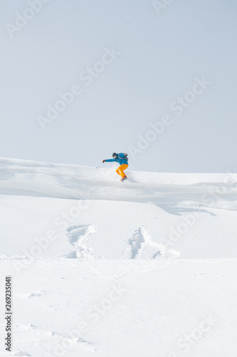 A snowboarder jumping off the cornice in a bright sunny day