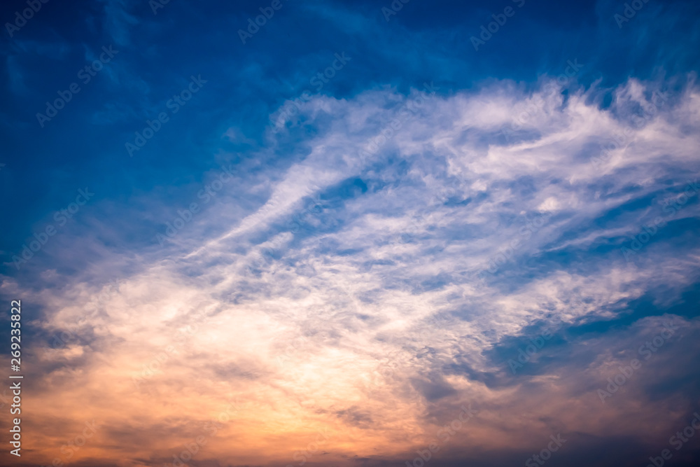View of cloudy blue sky with orange rays of light during sunset.