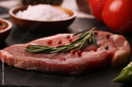 Raw pork meat steak with vegetables, peppers, tomato, salt, rosemary and spices cooking over stone table. Top view.