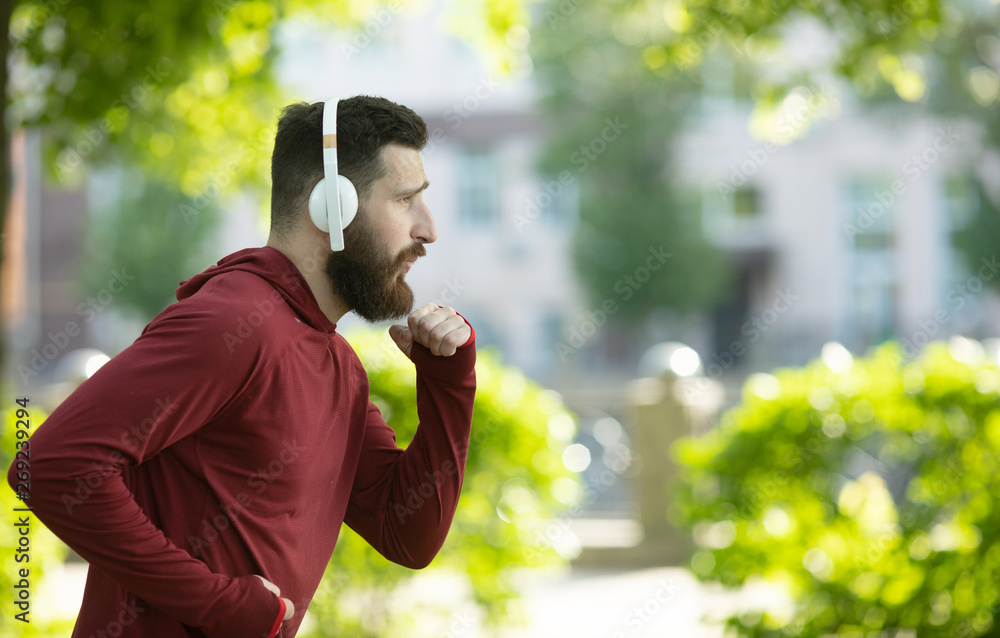 Fit bearded young man jogging through a park listening to music on his mobile phone. Fit bearded young man jogging through a park listening to music on his mobile phone.