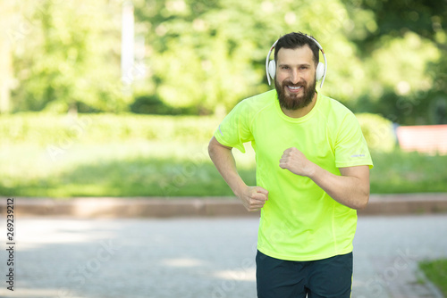 Fit bearded young man jogging through a park listening to music on his mobile phone.