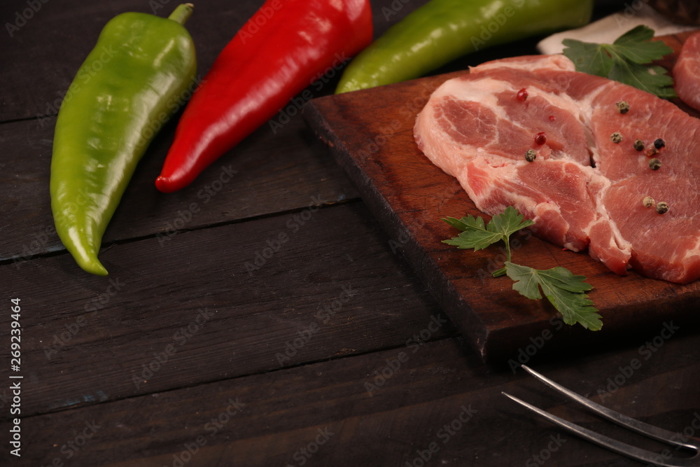 Raw pork meat steak with vegetables, peppers, tomato, salt, rosemary and spices cooking over stone table. Top view.