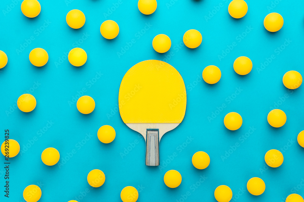racket and many balls for table tennis on turquoise blue background. flat lay image of many table tennis balls with tennis paddle in the middle. minimalist photo of yellow ping-pong equipment