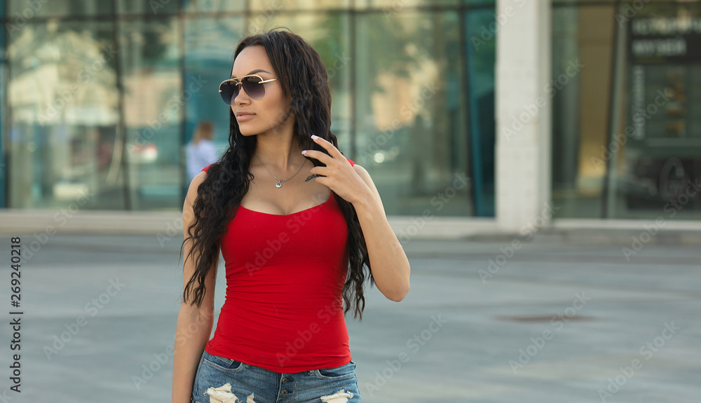 Φωτογραφία Attractive carefree gorgeous lady with bronze skin is posing in town, red top, in denim short shorts fit and slim body