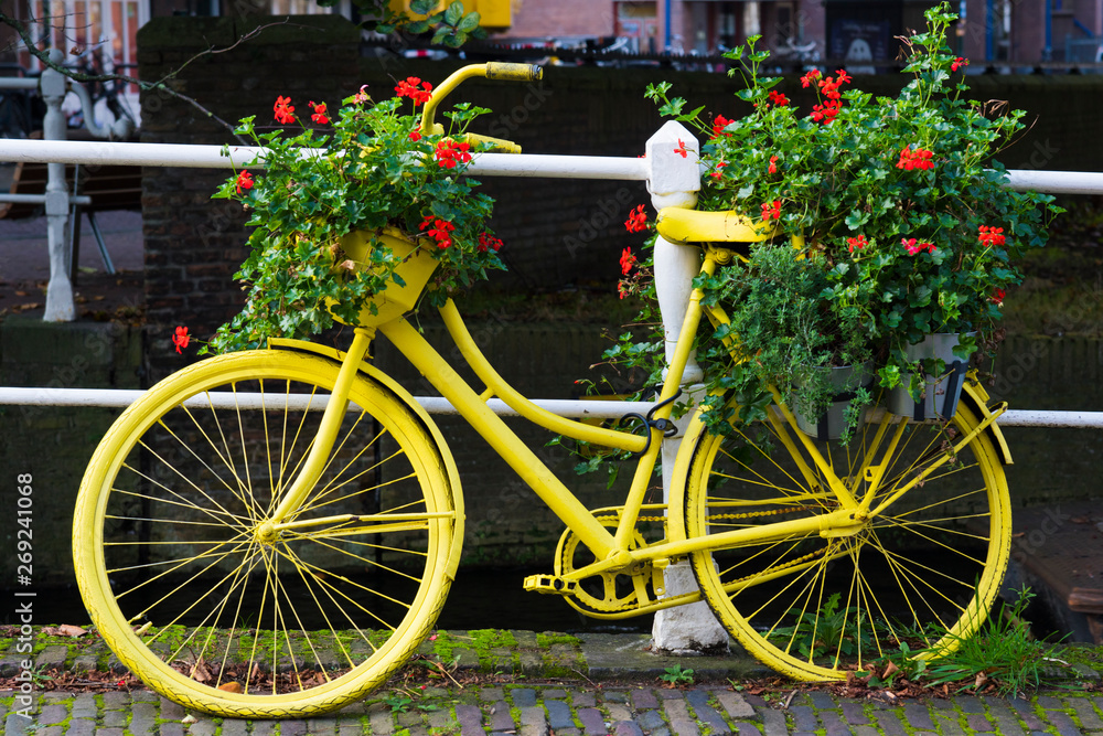 yellow painted bike against with flower pots, geraniums, against white fence along canal in Netherlands