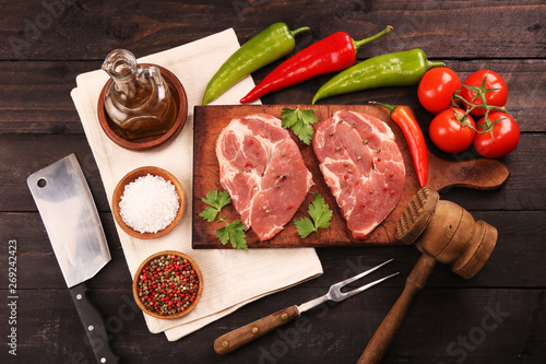 Raw meat. Raw pork steak on a cutting board with vegetables, peppers, tomato, salt and spices on a black background. Top view