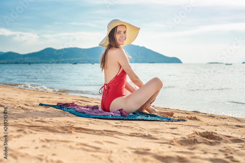 Beautiful woman in red swimsuit is sitting on the beach