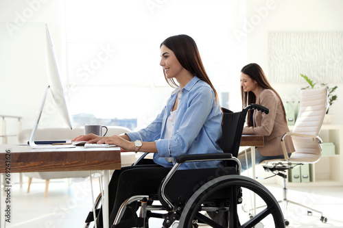 Young woman in wheelchair using computer at workplace