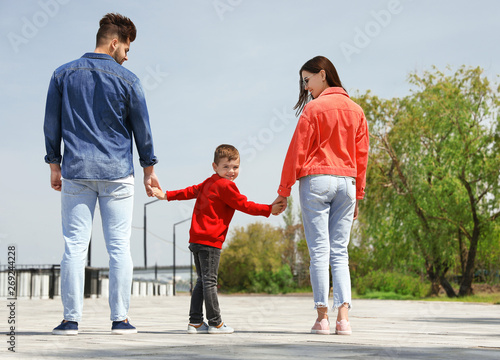 Happy child holding hands with his parents outdoors. Family weekend