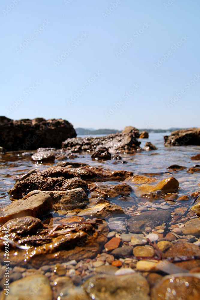 Exotic rocky beach with colorful stones, tropical blue sea with waves and foam. Beautiful natural environment, panorama, landscape. Idyllic seaside resort in summer season, paradise, amazing scene.