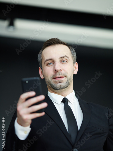 Low angle view of middle aged businessman with stubble holding smartphone and looking at camera