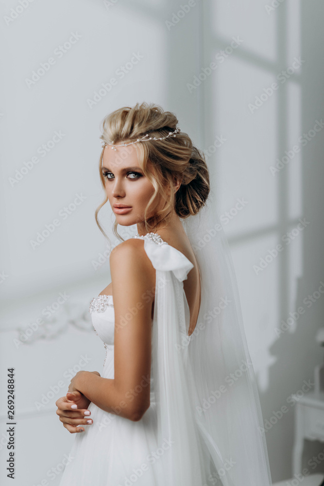 Bride with a beautiful hairstyle. Model blonde in a wedding dress in white interior Bride with a beautiful hairstyle. Model blonde in a wedding dress in white interior