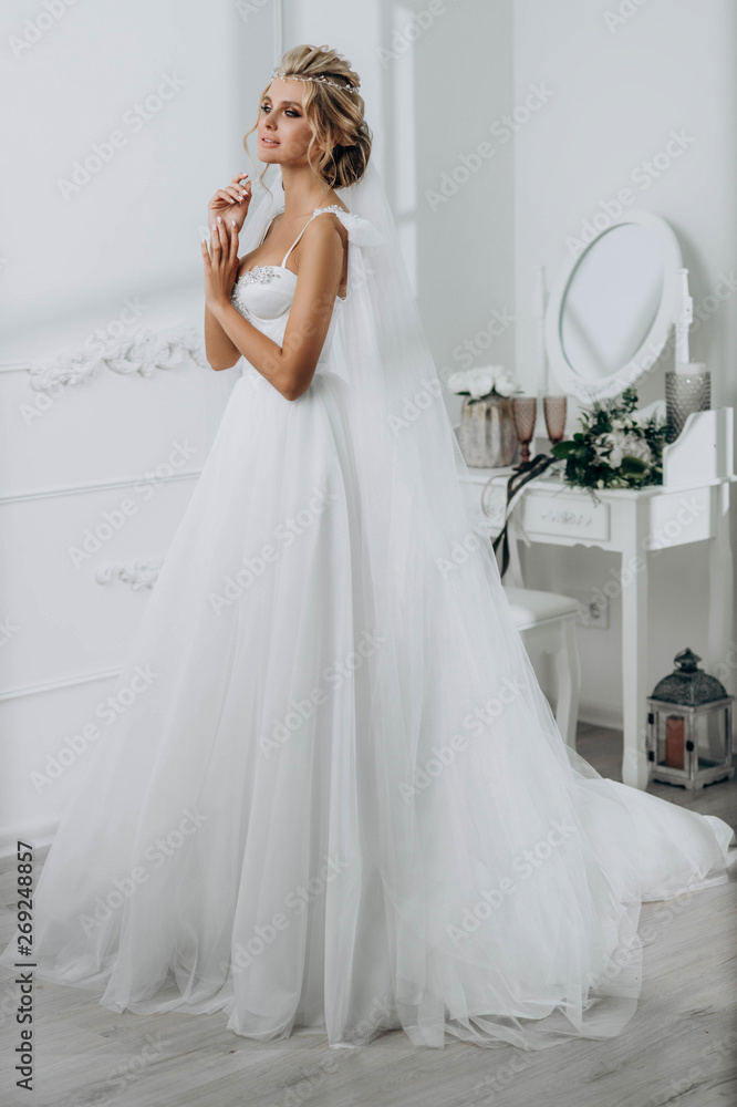 Bride with a beautiful hairstyle. Model blonde in a wedding dress in white interior Bride with a beautiful hairstyle. Model blonde in a wedding dress in white interior