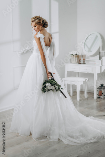 Bride with a beautiful hairstyle. Model blonde in a wedding dress in white interior