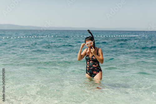 Woman getting ready to snorkel in sea. Female swimmer standing in water putting on snorkel and diving mask.