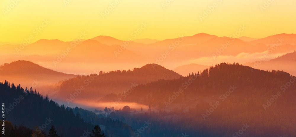 Landscape with beautiful mountains, fields and forests covered with morning fog. Panorama with interesting sunrise enlightens surroundings. Fantastic autumn day. Picturesque resort. Rural scenery.