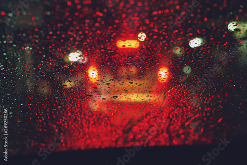 Drops Of Rain Drizzle on the glass windshield in the night. street in the heavy rain. Bokeh Tail light. soft Focus. Please drive carefully, slippery road. traffic jam car.