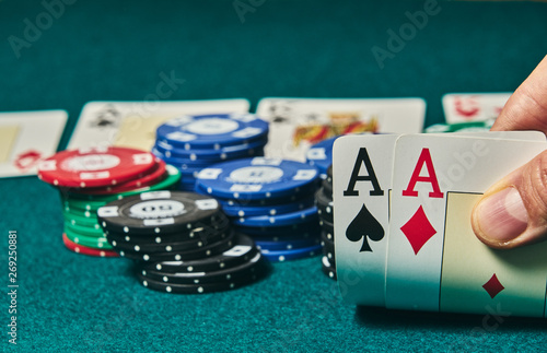 close-up of two aces held in one hand on the green game mat on the right side of the image to leave room for editing, other cards and poker chips are on the mat