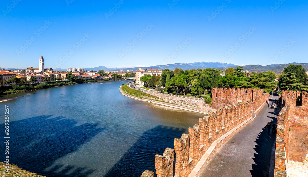 City of Verona on the banks of the river Adige, view of the Castelvecchio bridge, with mountains in the background and blue sky, Italy
