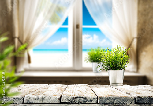 Wooden table of free space for your decoration. Small plant and summer window with sea landscape and beach. 