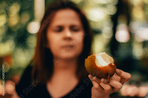 Closeup of a bitten pear held by a young woman with brown hair in a park or garden     Tasty and sweet snack with a girl in blurry background     Concept image for fruits as healthy deserts