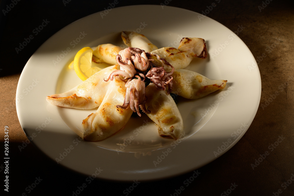 Grilled Calamari (Squid) with lemon and parsley on white plate on a plate in restaurant ready to be served Grilled Calamari (Squid) with lemon and parsley on white plate on a plate in restaurant ready to be served
