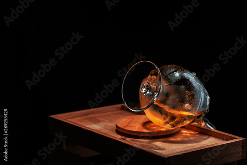  whiskey glass overturned and soaked up from cold ice from which follows drink  on a wooden support on a black background.