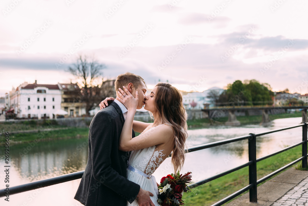 Naklejka premium the bride embraces the groom and kisses him on the bank of the river.
