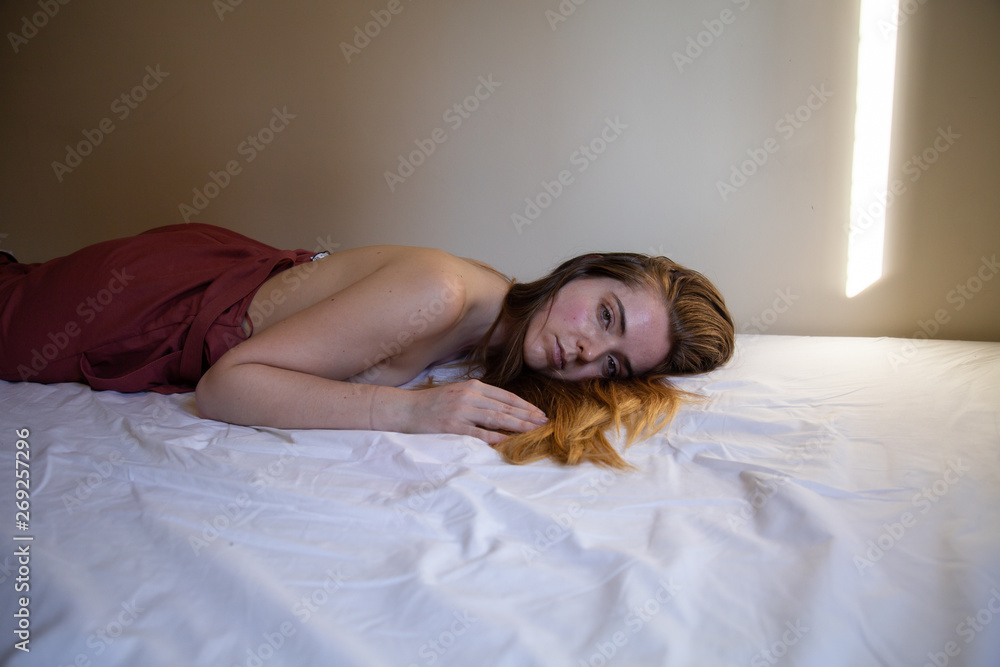 Girl with brown hair and bare chest, lying on her back in bed looking up. -  SuperStock