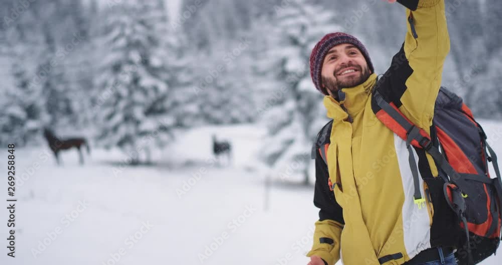 Happy charismatic tourist in the middle of mountain and snowy forest taking selfie with horses, using the smartphone Happy charismatic tourist in the middle of mountain and snowy forest taking selfie with horses, using the smartphone