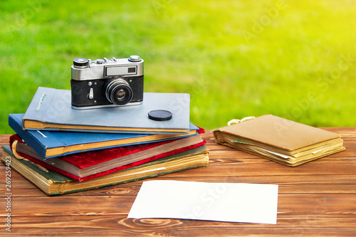 Old photo album with photos on a beautiful brown wooden table on the background of nature and old cameras