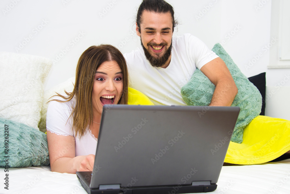 Cute young couple watching horror, comedy or chat on lap top in bed, female model size plus woman, male model bearded long hair man, relationship concept