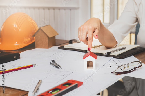 Business, architecture, building construction and real estate concept. Female real estate agent presenting a house model. Young female architect pointing model of house in office.