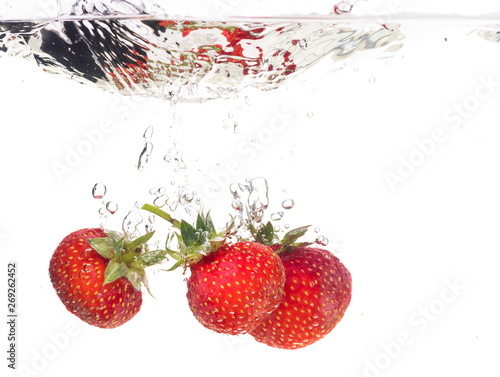 Red fresh strawberries thrown into the water, under water. Spat and splash