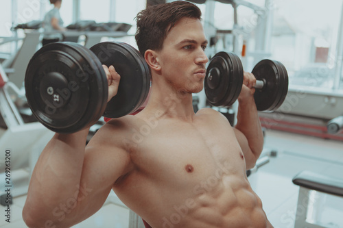 Close up of a sexy ripped strong male athlete working out with heavy dumbbels at the gym. Handsome healthy powerful male bodybuilder exercising with weights