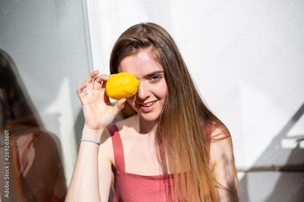Young happy pretty female in casual summer dress sitting on terrace and covering eyes with ripe lemons Young happy pretty female in casual summer dress sitting on terrace and covering eyes with ripe lemons