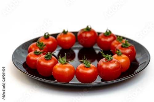 Tomatoes in a black plate isolated on white background. Composition of red tomatoes on a white background. Place for text © Maksym