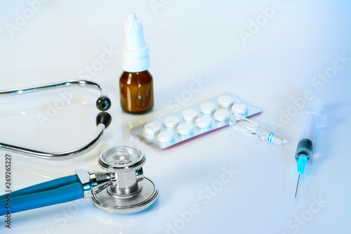 Stethoscope or phonendoscope on a doctor's white desk with syringe, nosal spray, medicines. Treatment of cold or flu photo