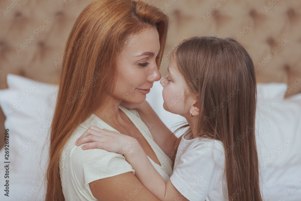 Close up of a  beautiful long haired woman touching noses with her cute little daughter. Adorable little girl rubbing noses with her charming mother. Love, affection, mothers day concept