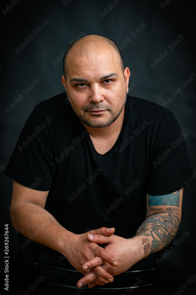 Emotions, man in black t-shirt sitting on chair with indifferent look isolated on black background.