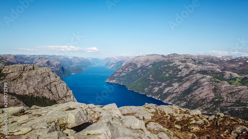 Endless view on Lysefjorden seen from Preikestolen, Norway. Steep cliffs join the water. Few ships on the water. Clear and bright day. Barren rocks on the top of the cliffs, partially snow-capped