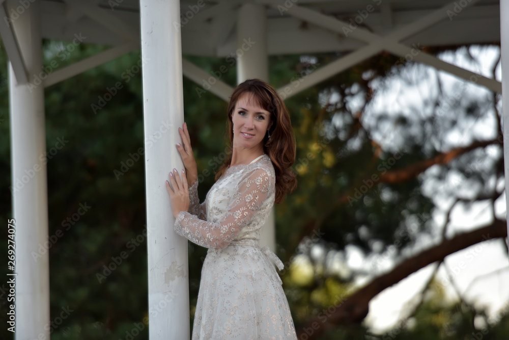 Naklejka premium A woman in a white dress in the park at the gazebo