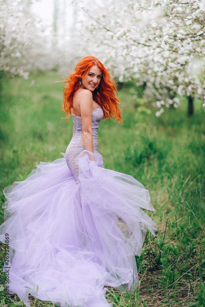Happy young red-haired woman enjoying spring in blossoming garden