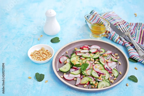 Light salad of crispy radish, cucumber and mint leaves with citrus dressing on a brown plate. Sprinkled with pine nuts.