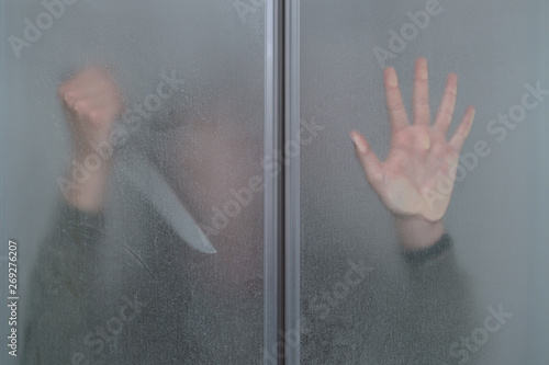 girl with a knife in hand is hiding behind a dirty glass door