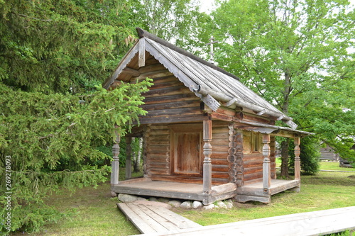 Old wooden house against the background of green grass and trees in the museum of wooden architecture. © Svetlana