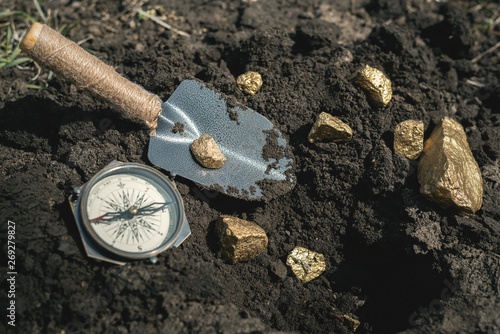 Golden nuggets, compass and showel on a ground. Treasure hunt concept background.