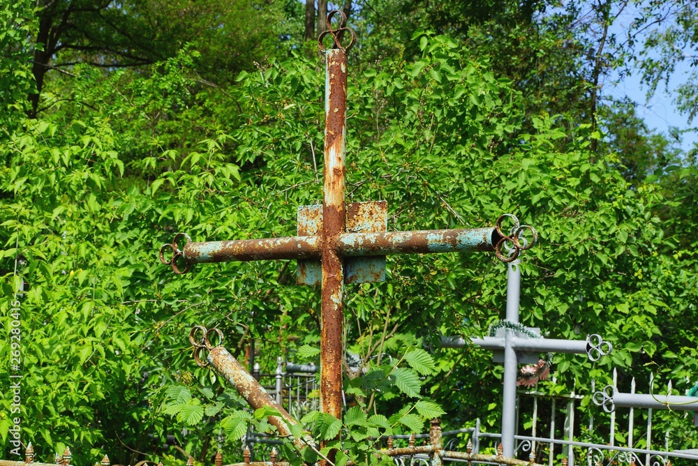 old rusty iron cross overgrown with green vegetation at a cemetery