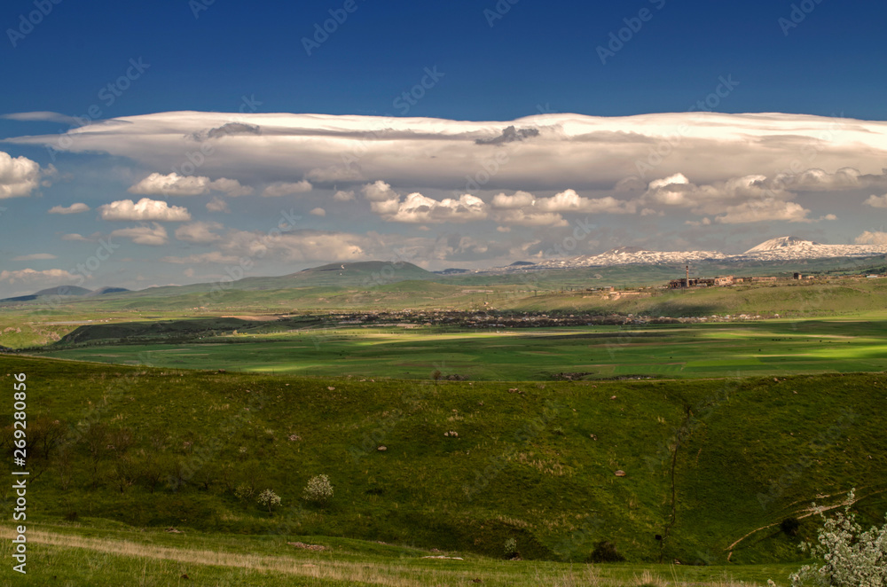 Spring blue sky with occasional turbulent cloud with Cumulus clouds approaching the villages and the valley of the mountains of Geghama mountain range in Armenia
